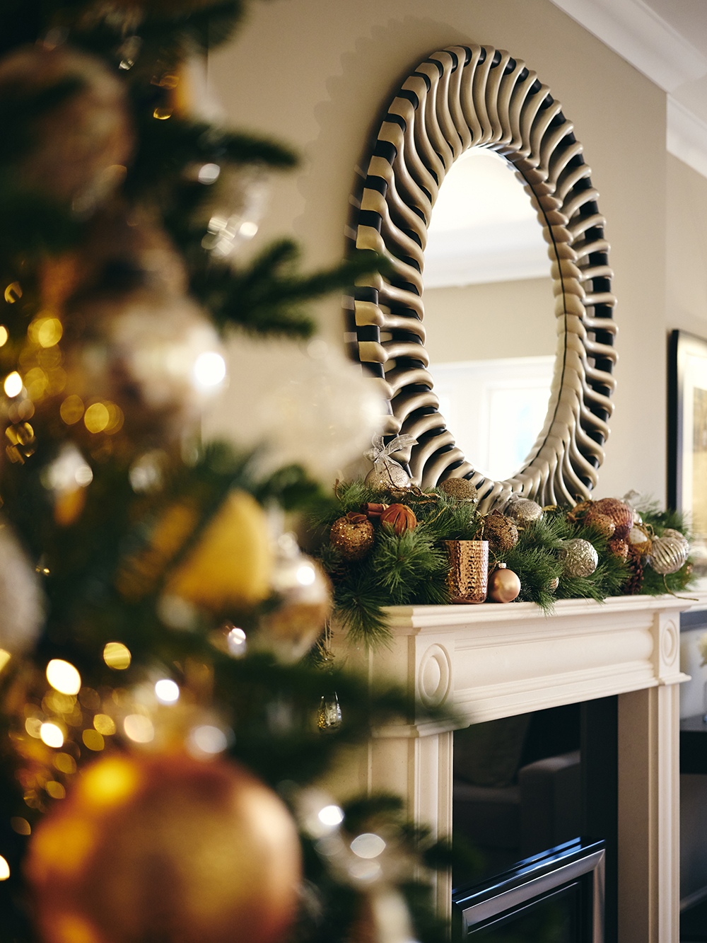 Redrow | Inspiration | A circular mirror above a festive fireplace arrangement, seen behind a Christmas tree in the foreground