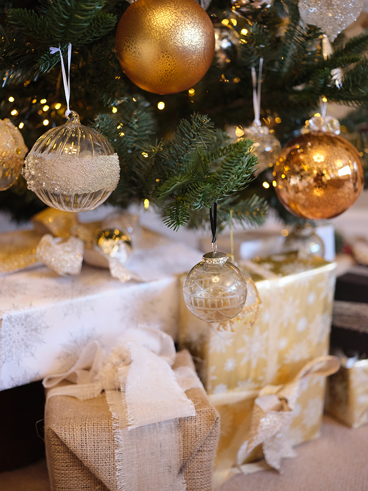 Redrow | Inspiration | The base of a Christmas tree hung with gold and silver baubles, above a collection of wrapped gifts